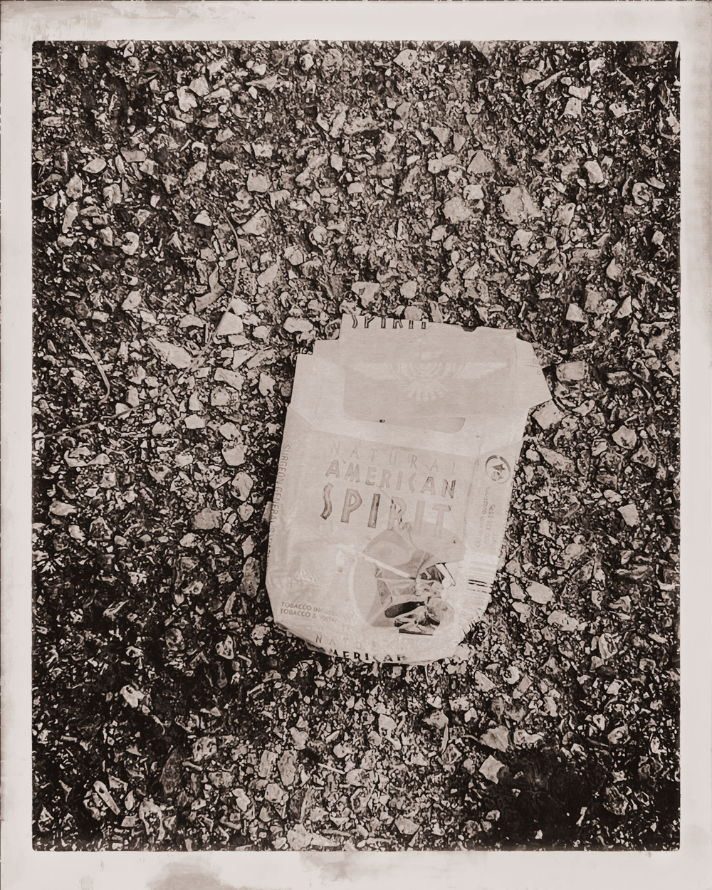 American Spirit cigarette pack on asphalt pavement. Vintage black and white filter applied.