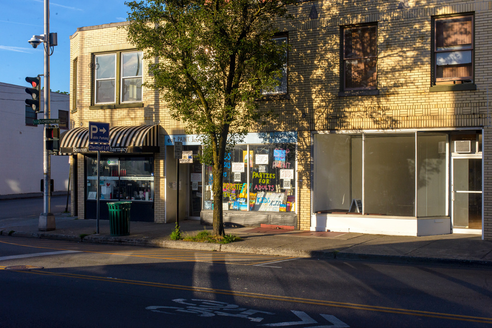 Storefronts illuminated by early morning sun and sunlight reflected onto the sidewalk and street by window glass.