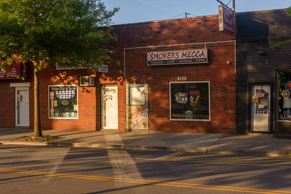 Storefronts illuminated by early morning sun and sunlight reflected onto the sidewalk and street by window glass.