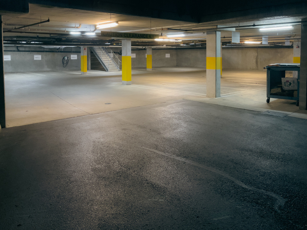 Parking garage entry with grid of square columns in the distance, fluorescent lighting on the ceiling. Garage is empty.