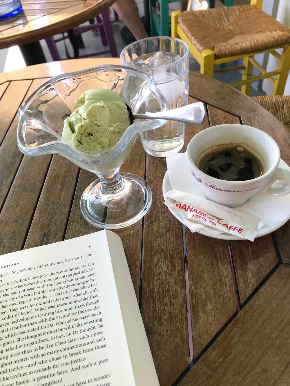 A cup of coffee and a bowl containing a scoop of ice cream on a cafe table. The upper part of the right page of a book is also visible.