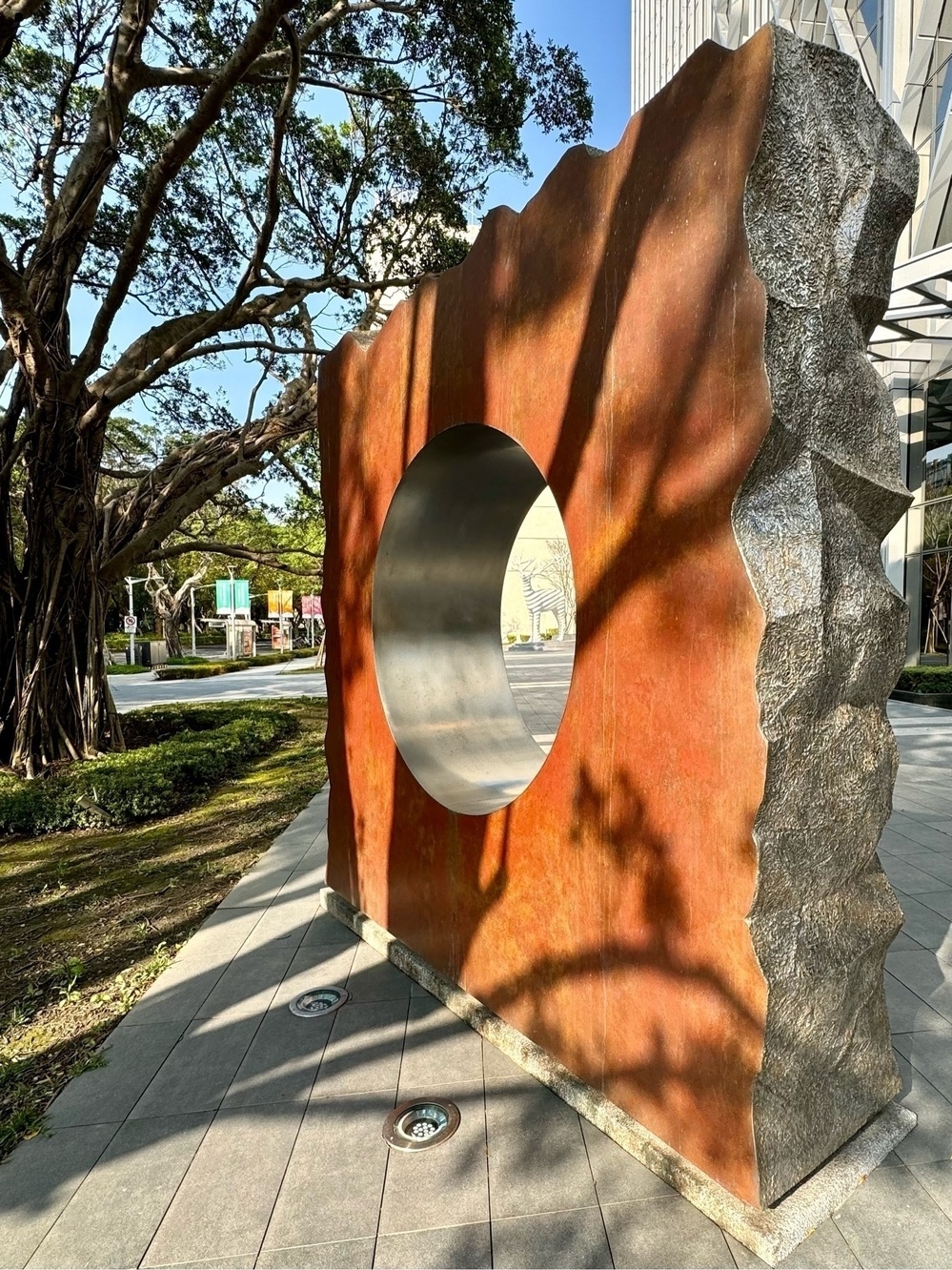 A stone tablet, with a brown surface and a hole cut in its centre, stood at an oblique angle facing away from the camera, with a white reindeer statue in the distance, appearing through the hole.