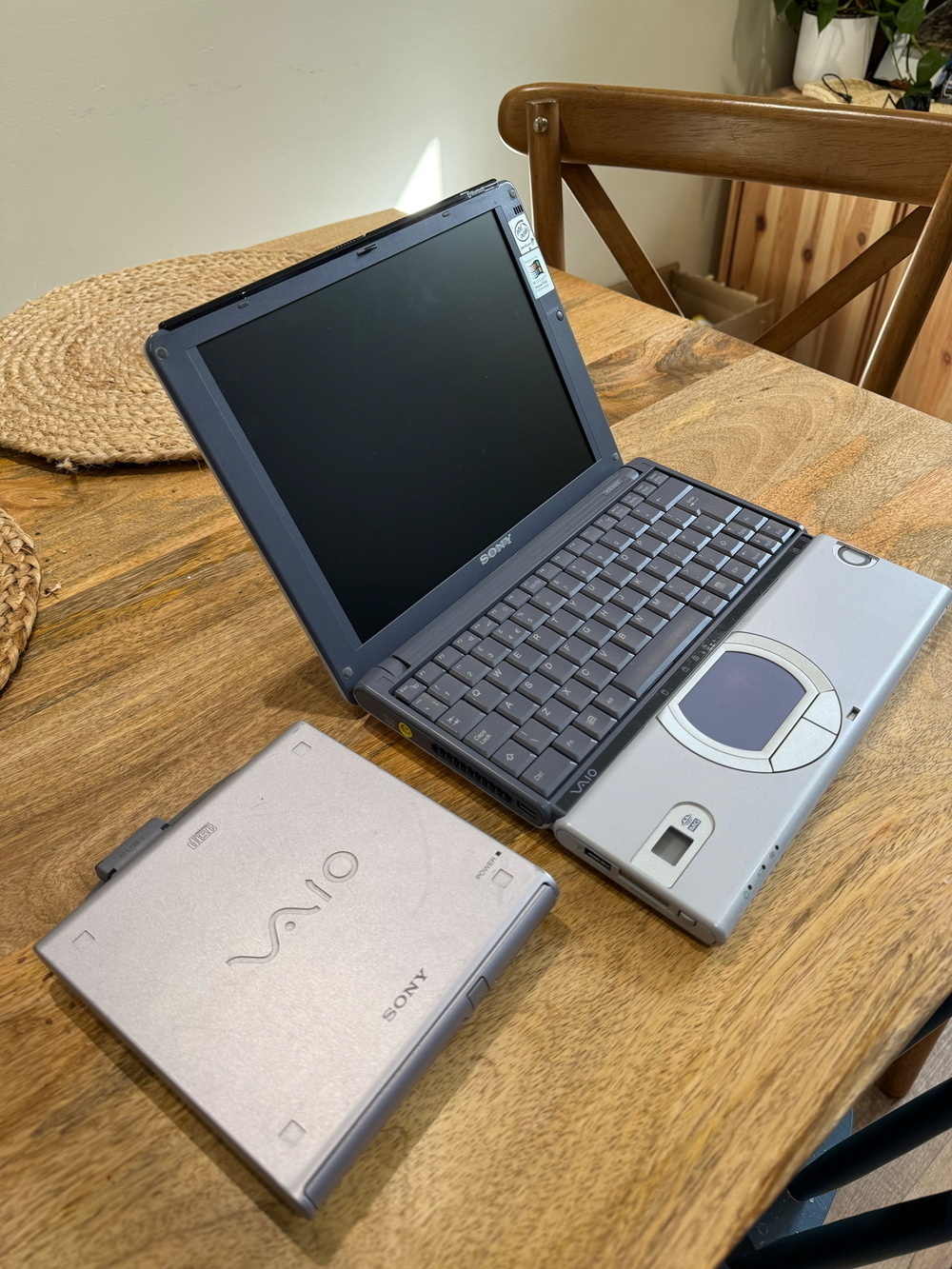 A vintage Sony VAIO laptop on a wooden table with an external disc drive placed next to it.