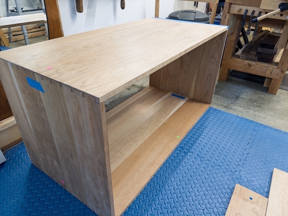 A wooden cabinet is placed on a blue rubber mat in a workshop.