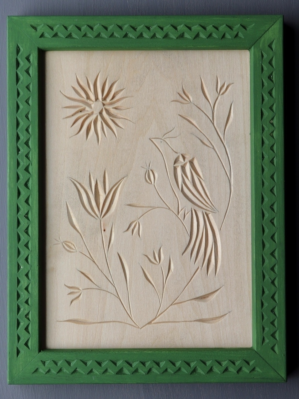 relief carving of a bird perched among flowers gazing at the sun; green frame carved with weaving triangles