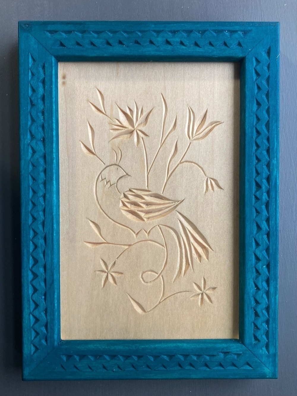 chip carved bird in vined flowers, teal-blue frame carved with woven triangles