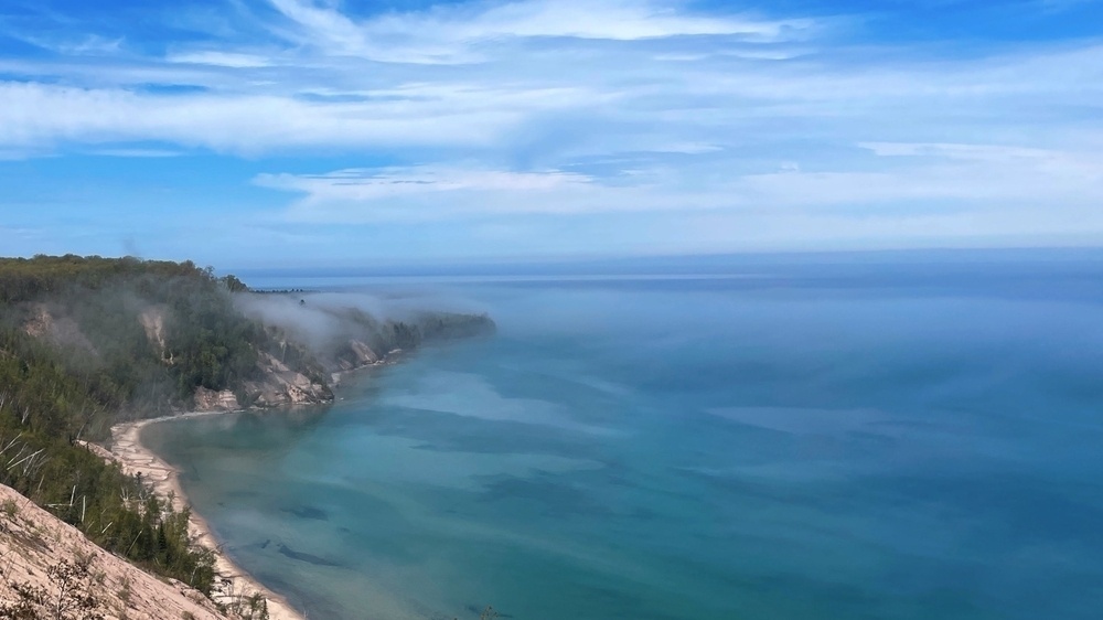 Looking out over the  lake with a sandy forested shore below covered in trees scattered with the last of the morning fog