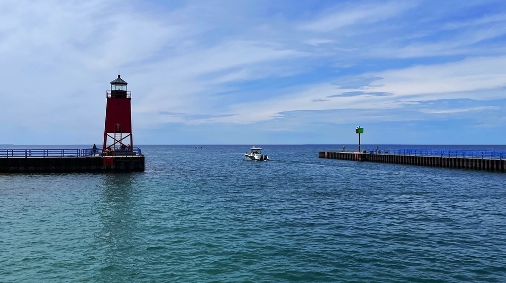 Looking out onto the lake past a lighthouse and jetty, a boat heading out