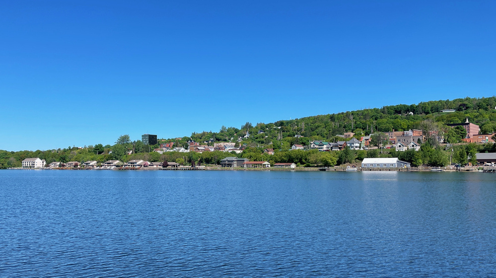 A view across the Keweenaw waterway of houses against a low green mountain
