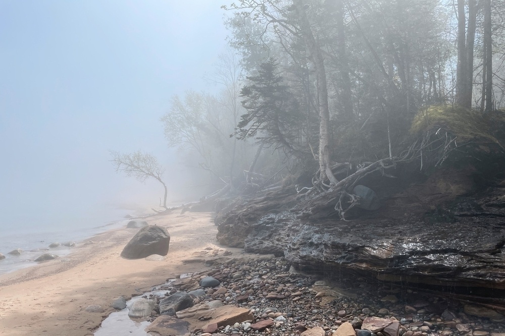 a beach along the shore of lake superior on a foggy (but also sunny) day.