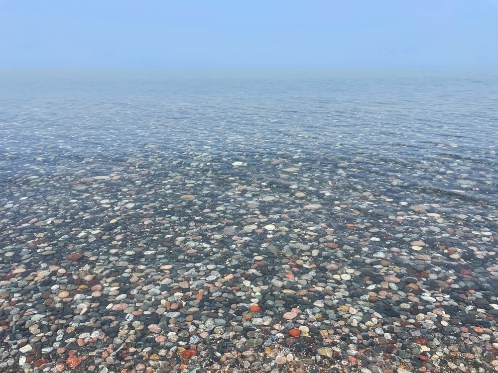 Clear and shallow lakeshore waters in which a vast bed of multicolored stones can be observed.