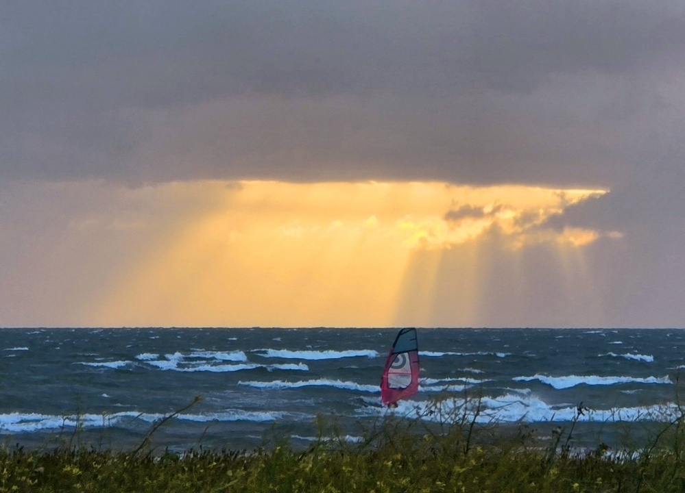 windsurfer surfing the waves against a backdrop of evening sunset rays beaming down on the horizon