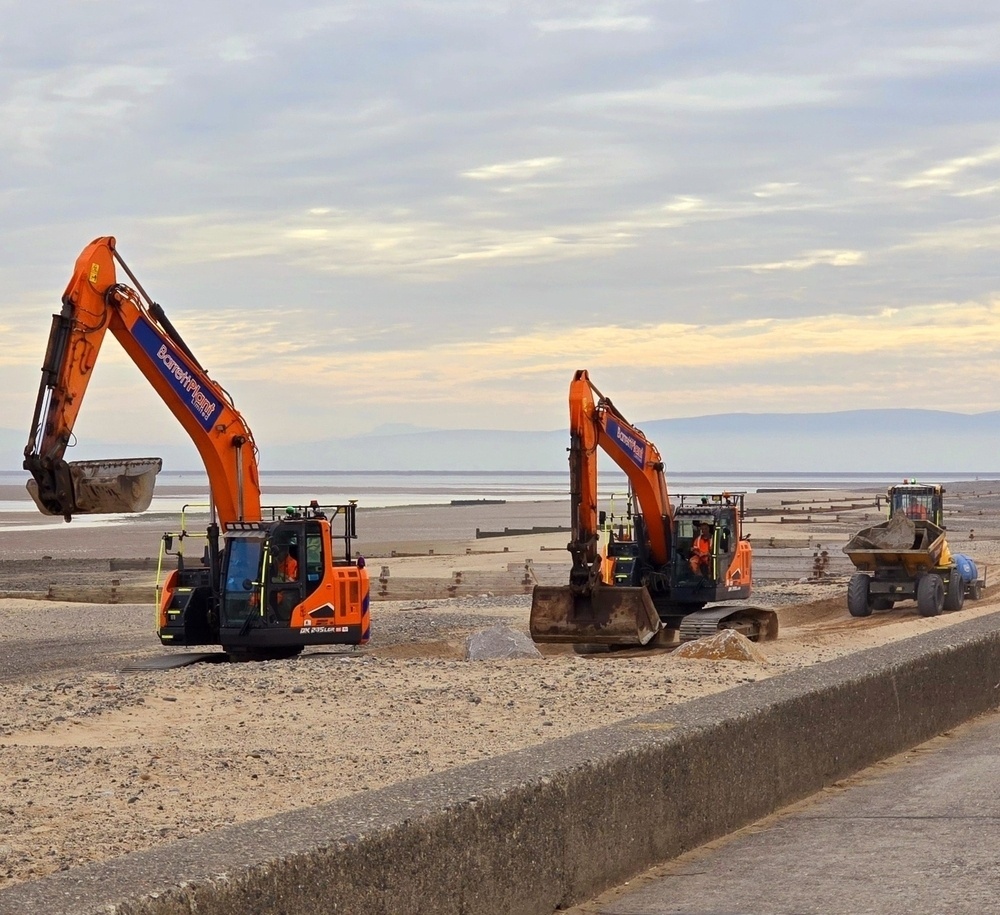 Three large fork lift machines driving on the beach in a line 