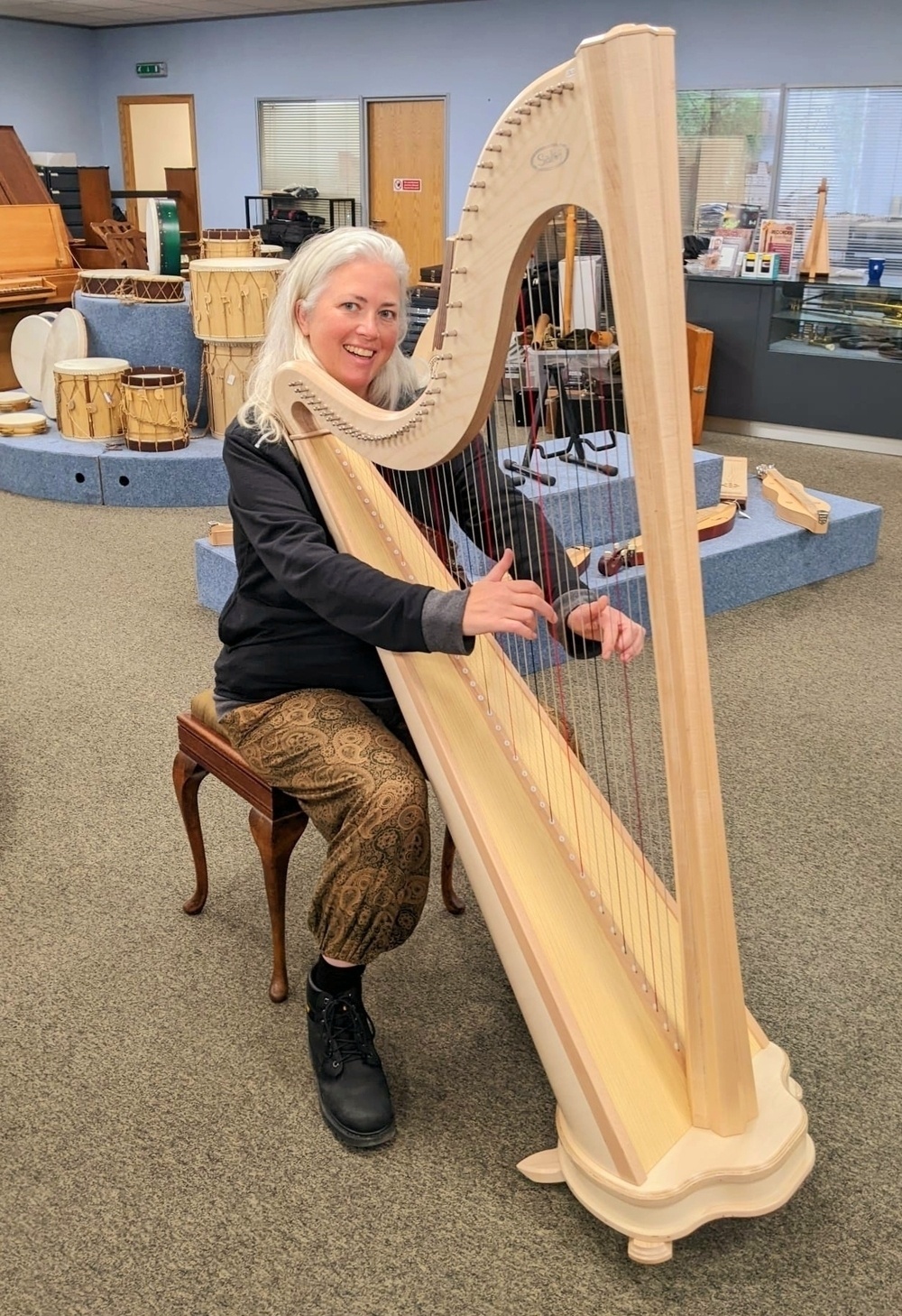 Holly playing a large harp in a music shop