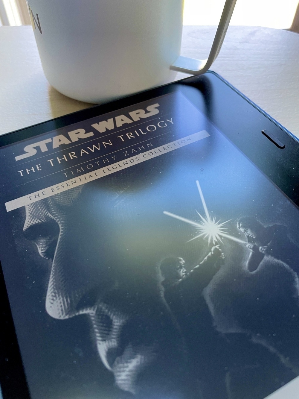 Photograph of a wood table with coffee cup and open ebook cover of The Thrawn Trilogy