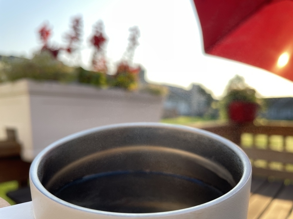 Closeup view of a coffee cup with a sunny scene of flowers and a red umbrella blurry in the background