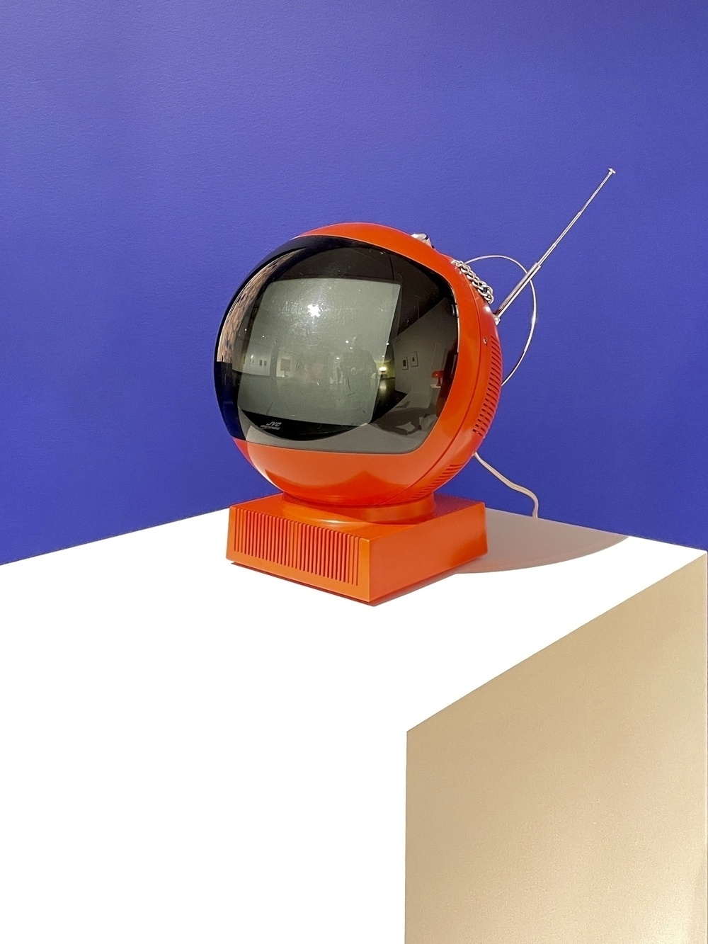 Red circular 1970’s television on a white platform against a blue background 