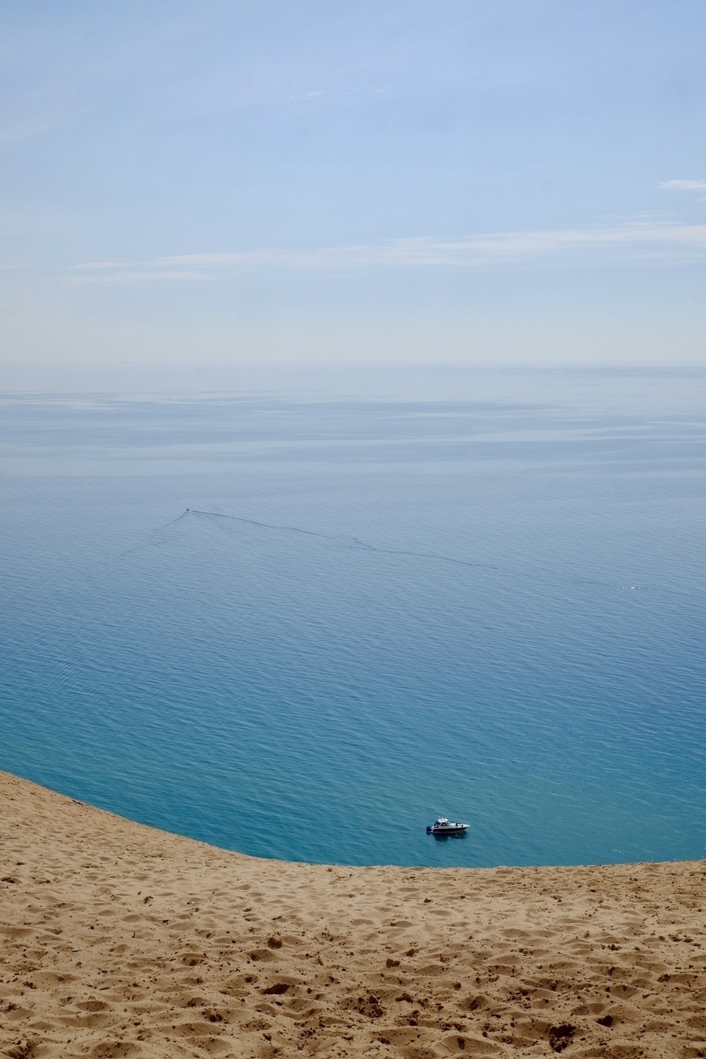 Portrait view of a blue sky meeting the similarly blue colored water of Lake Michigan with a boat floating at the bottom with sand in the foreground