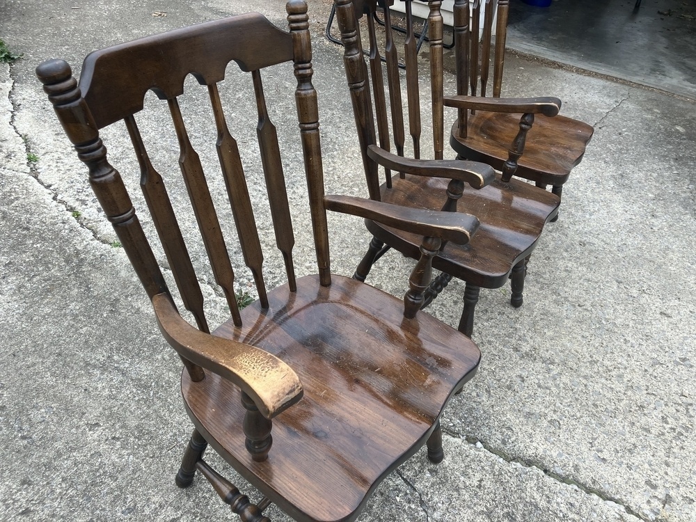 Auto-generated description: Three wooden chairs with armrests are aligned in a row on a concrete surface.