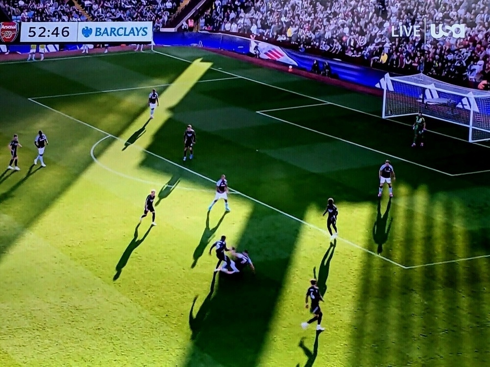 Players and their shadows  on a green football pitch near sunset