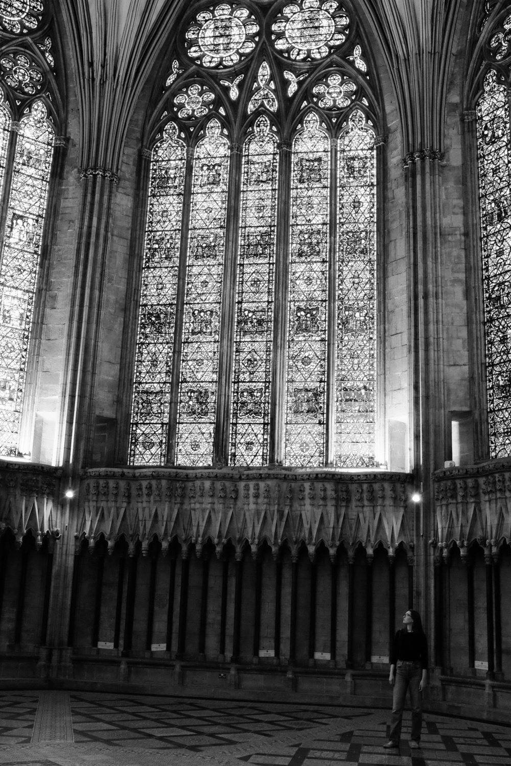 Jacqueline gazes up at a stained glass window that stretches above her. Black and white.