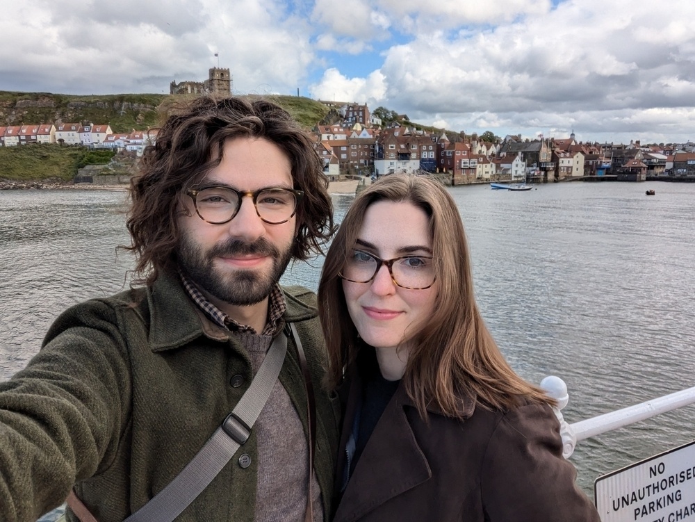 A selfie of Jacqueline and me, with Whitby harbor in the middle ground and St. Mary's church on a hill in the background.