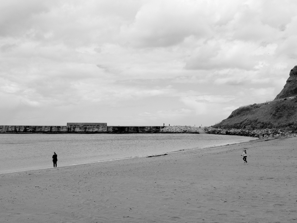 A young girl runs on the beach toward her mother, who stands at the edge of the water.