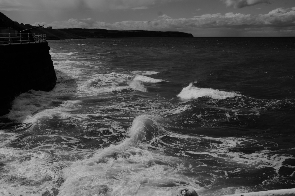 Waves break against a sea wall, in black and white