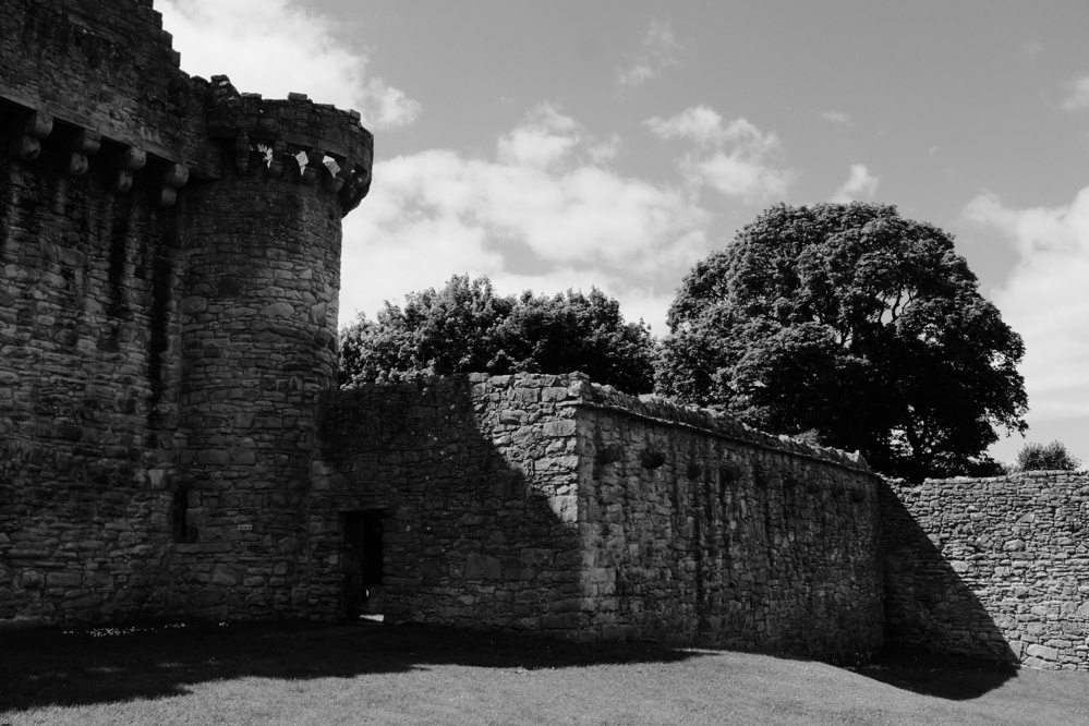 A tower at the corner of a castle building in black and white, casting shadows on the lower wall.