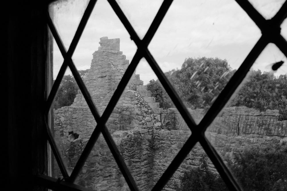 A view of what used to be the roof wall of the castle in black and white, viewed through a window with grates.