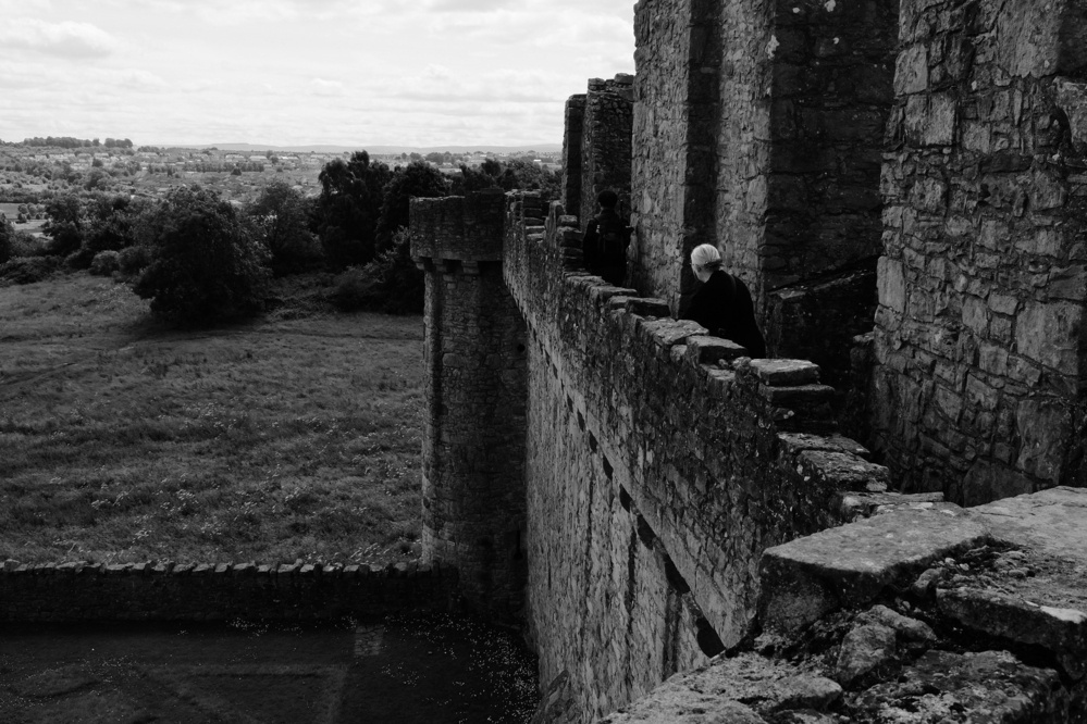 A woman stands on a wall of the castle, gazing into the distance, in black and white.