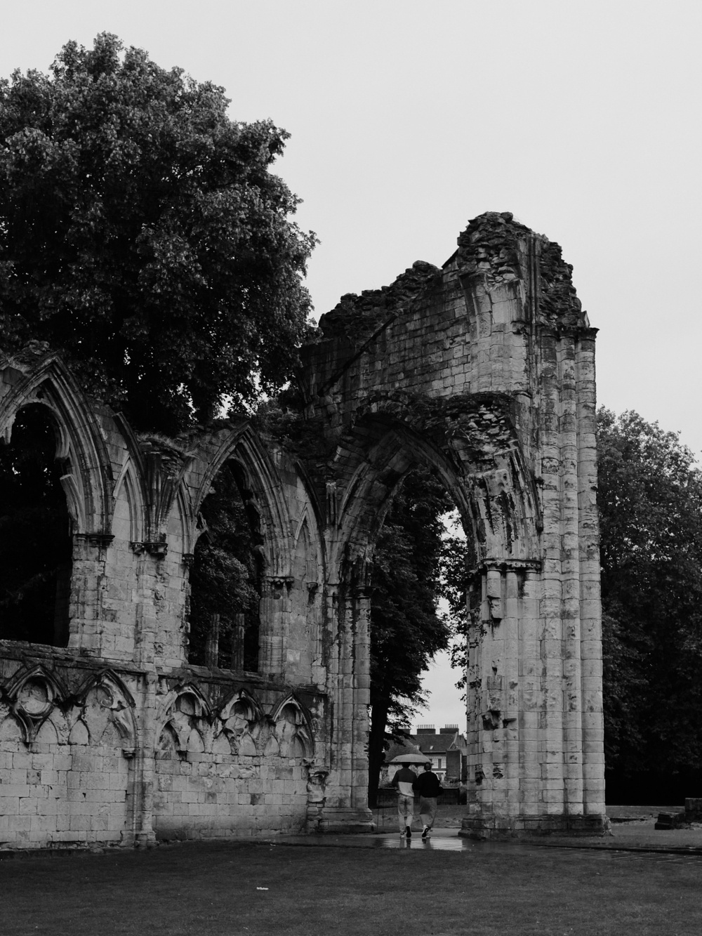 A couple, an umbrella overhead, pass beneath the dilapidated archway of what was once a Gothic monastery.