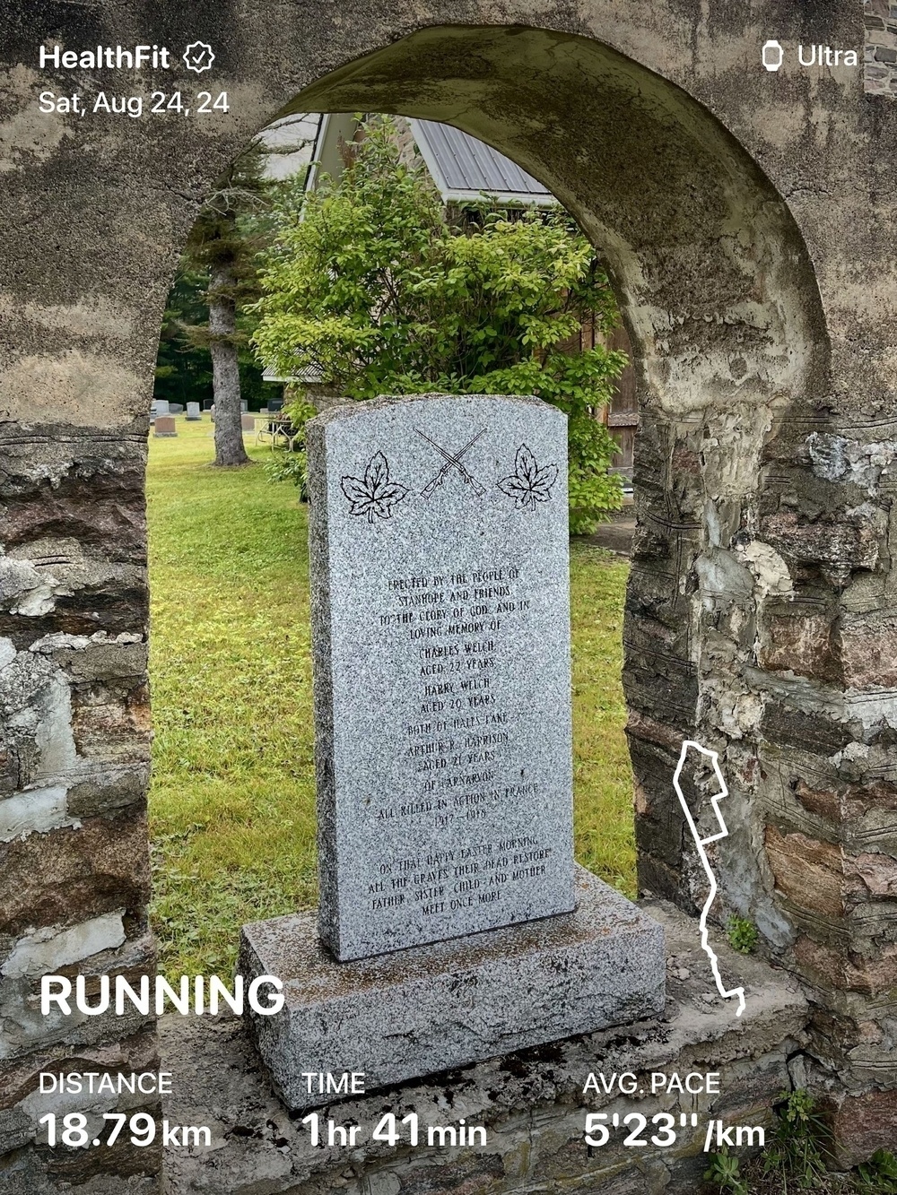 A stone monument with inscriptions stands within an archway, surrounded by a grassy area and trees, while a running app overlay displays workout details.