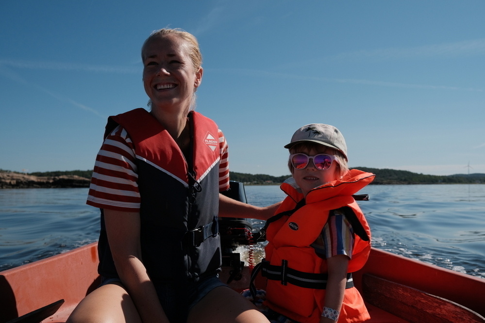 Kvinna och barn sitter tillsammans i en liten båt och styr med hjälp av utombordaren. 