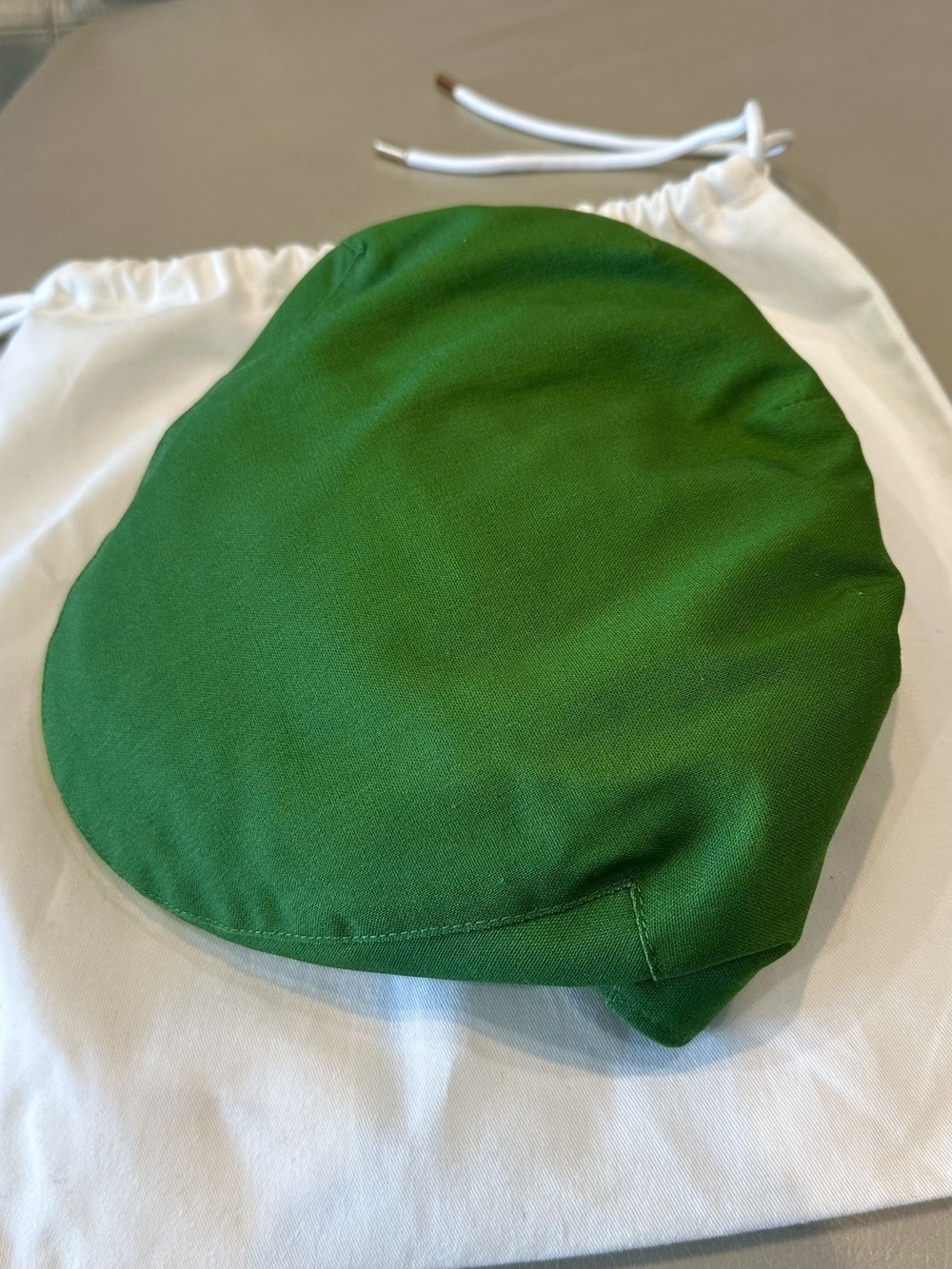 A green flat cap laying on the white cotton bag it came in.