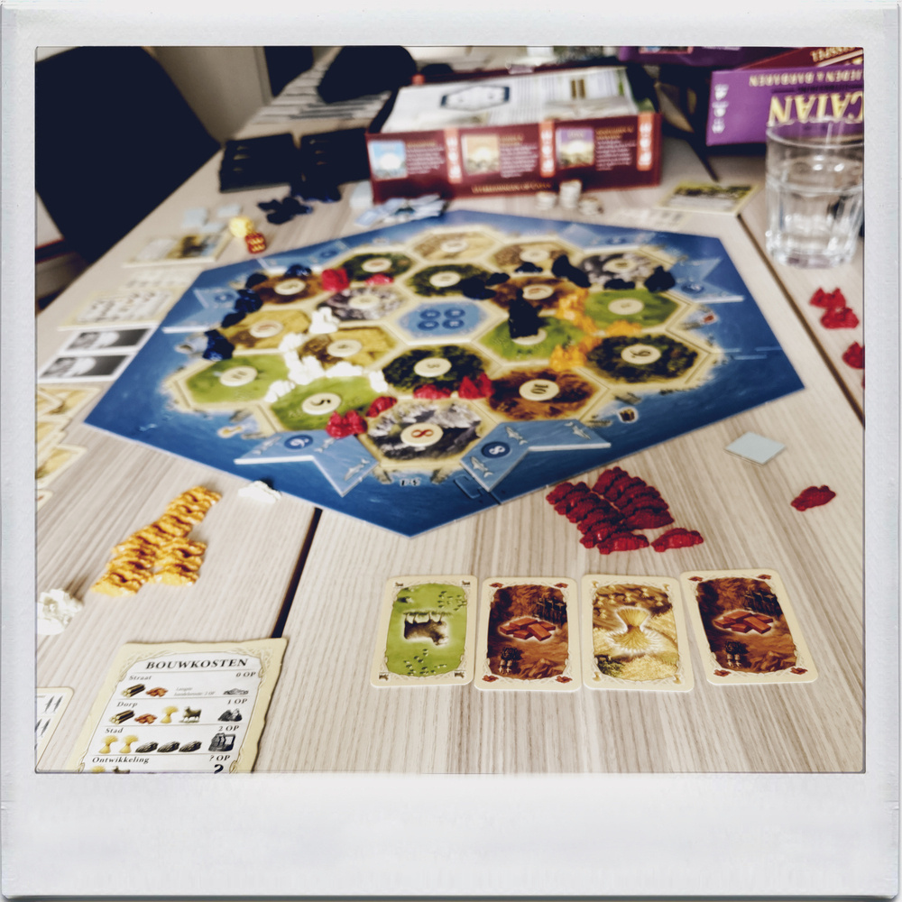 Auto-generated description: A board game with hexagonal tiles, resource cards, and various tokens is set up on a wooden table.