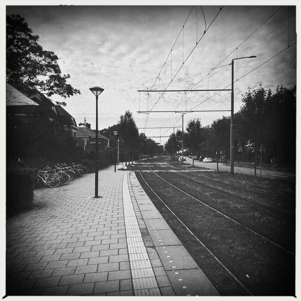 A quiet, empty street with tram tracks running alongside paved walkways and bicycles parked near lampposts.