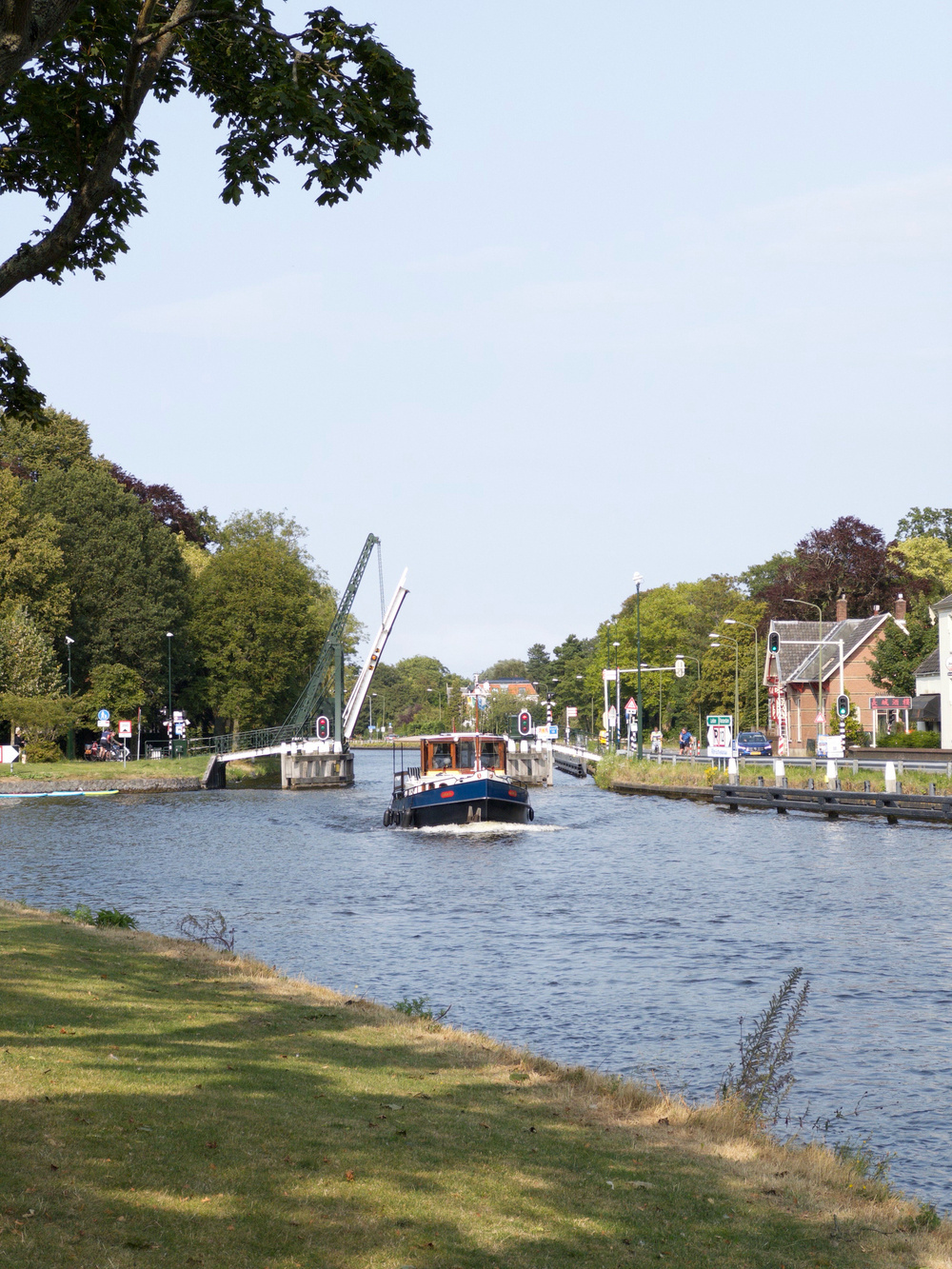 Auto-generated description: A boat navigates down a peaceful river flanked by green banks and a raised drawbridge in the background.