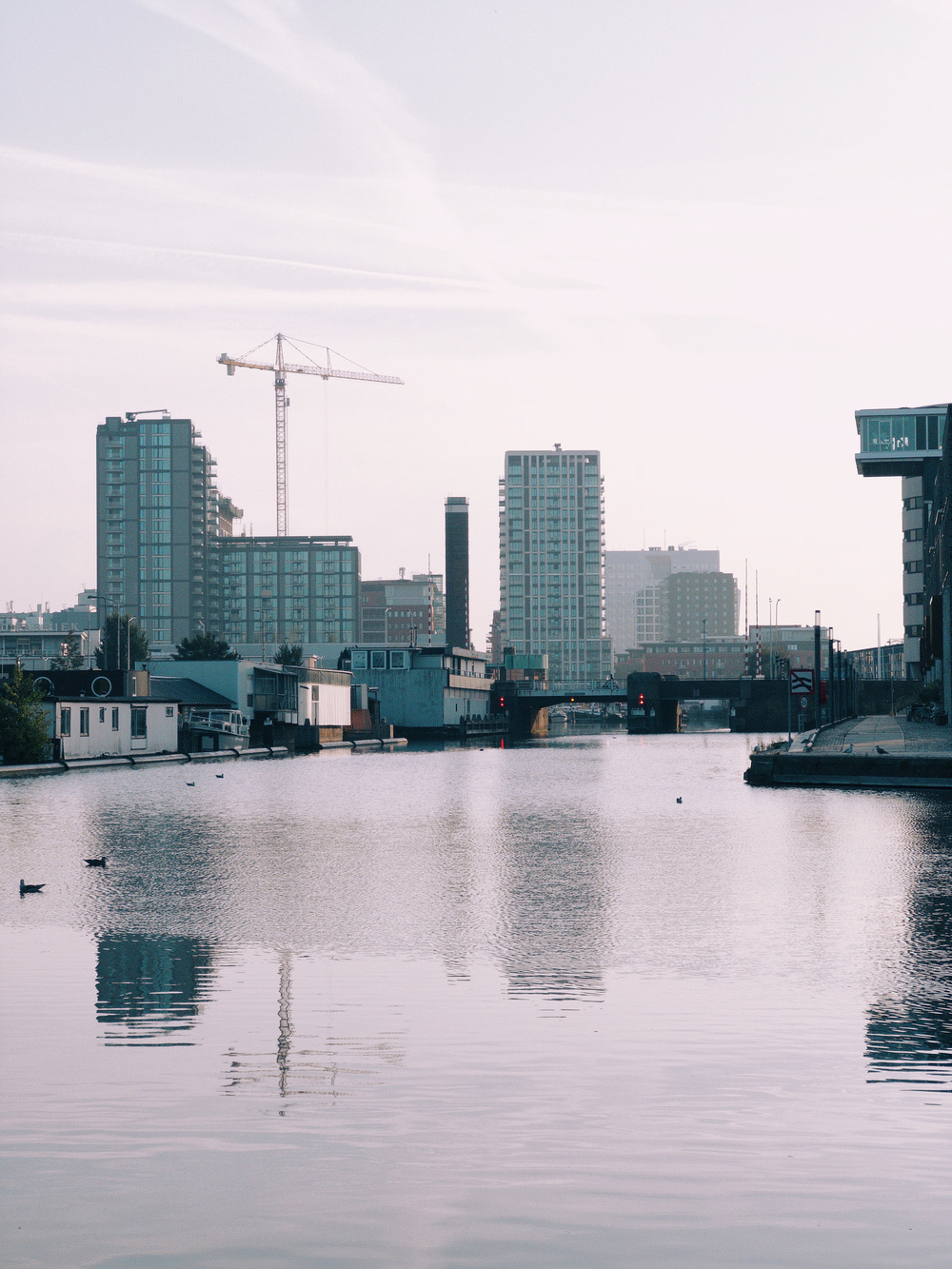 Skyline of modern buildings and a construction crane reflected in a calm canal in The Hague, Netherlands.