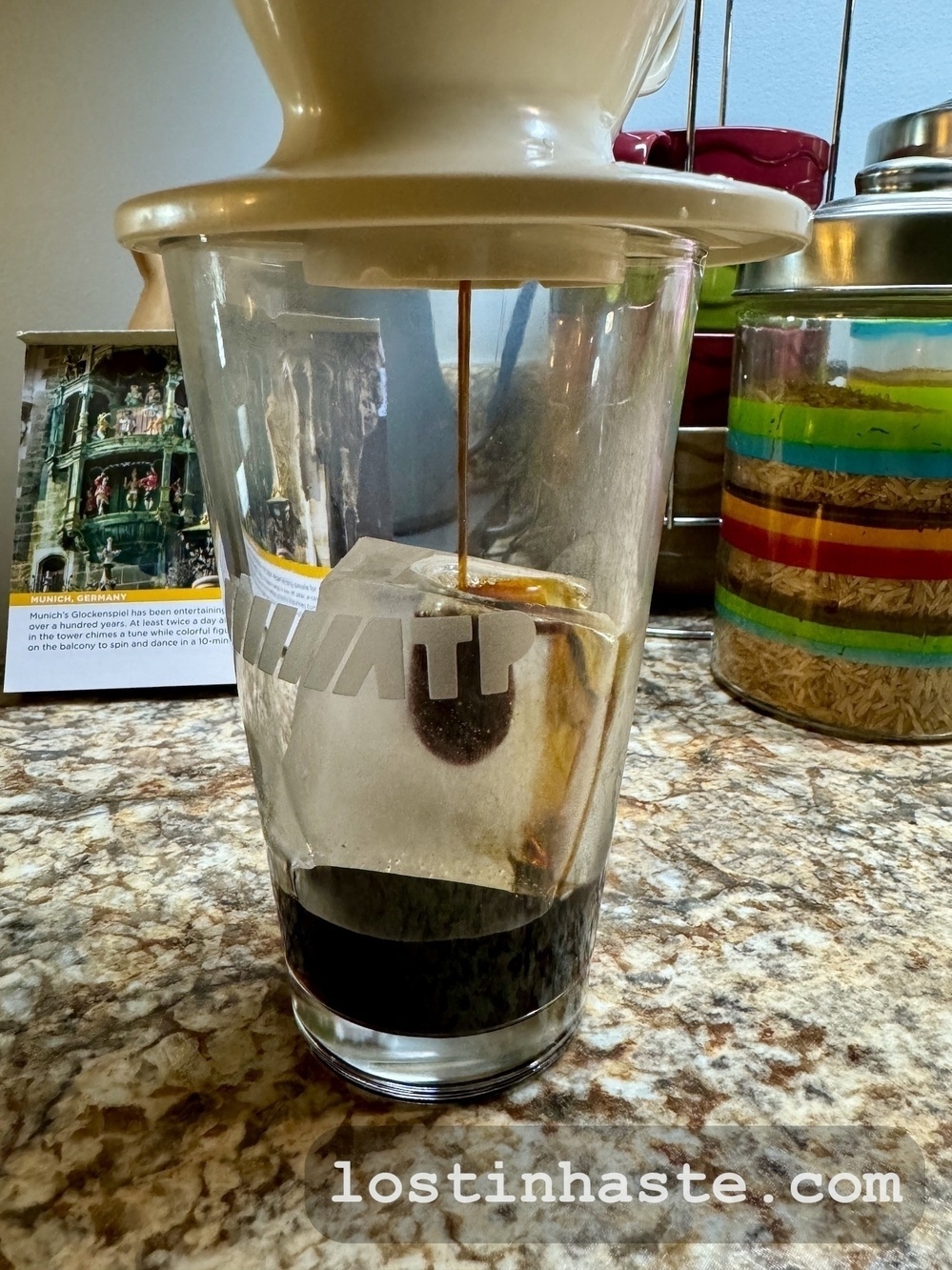 A coffee filter drips into a glass carafe on a kitchen countertop, flanked by colorful canisters. Website address 'lostinahaste.com' is visible.