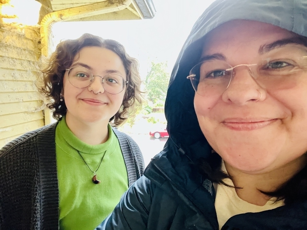 Two people on a porch smiling, wild smashing rain behind them but you can't make that out because cameras. 