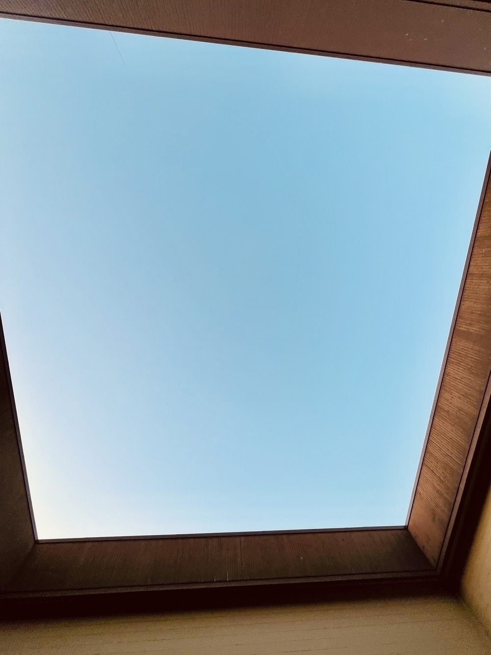 Looking up through the roofs of four buildings that touch each other and sit over four streets. All you can see are the four golden brown wood walls of the roofline, some of the bricks below, and a rectangle of blue sky. 
