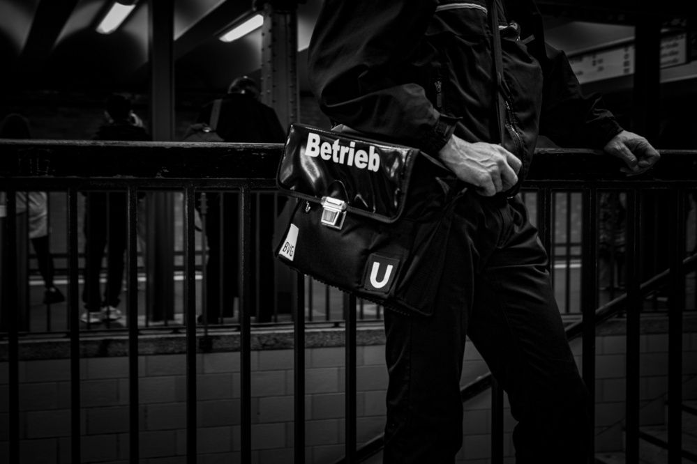 Eine Person, die an einer U-Bahn-Station steht, eine Uniform trägt und eine Tasche mit der Aufschrift "Betrieb" hält.