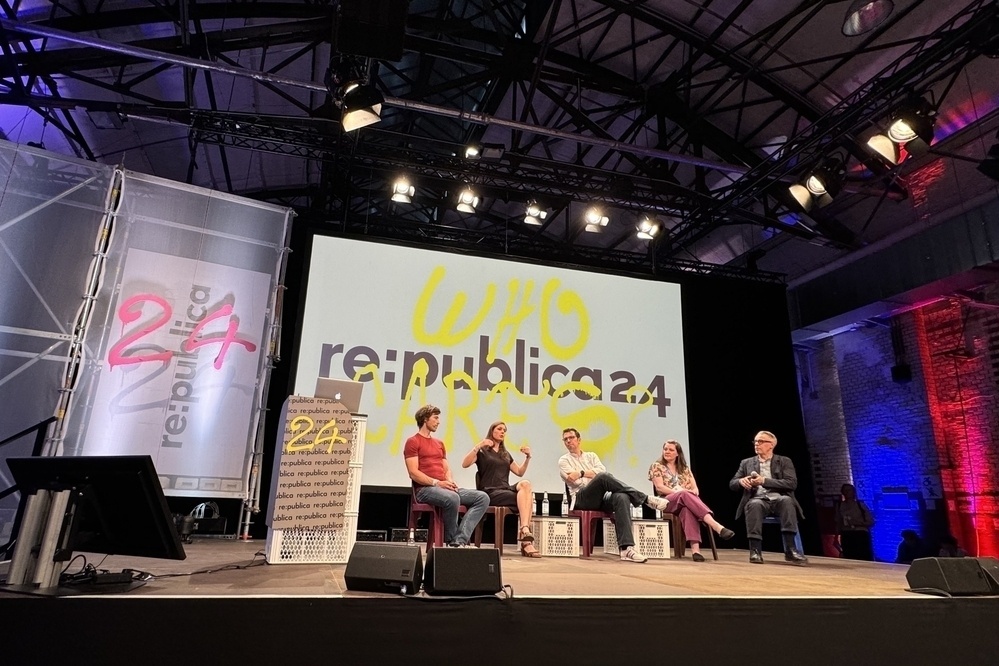 Eine Podiumsdiskussion auf der re:publica 24-Konferenz mit fünf Personen auf der Bühne, einem großen Bildschirm hinter "re:publica 24" und "WHO CARES?" und Bühnenbeleuchtung über dem Kopf.