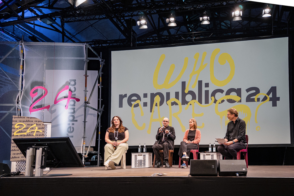 Vier Diskussionsteilnehmer sitzen auf der Bühne der re:publica 24-Konferenz unter einer großen Leinwand mit der Aufschrift "WHO CARES?" In gelbem Text.