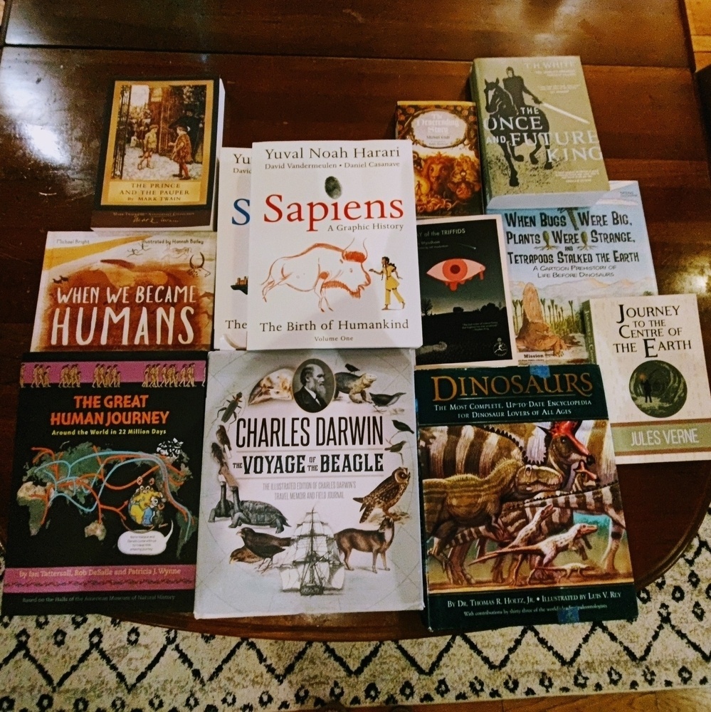 A pile of books on a table. Books are a variety of nonfiction and fiction texts including titles like the “Once and Future King” and “Charles Darwin and the Voyage of the Beagle”