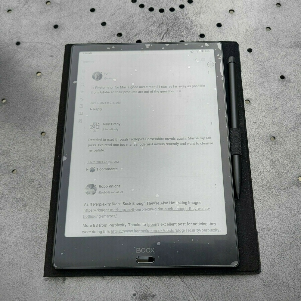 Auto-generated description: A tablet with an attached stylus displays an e-book reader application with text and comments, resting on a textured surface.