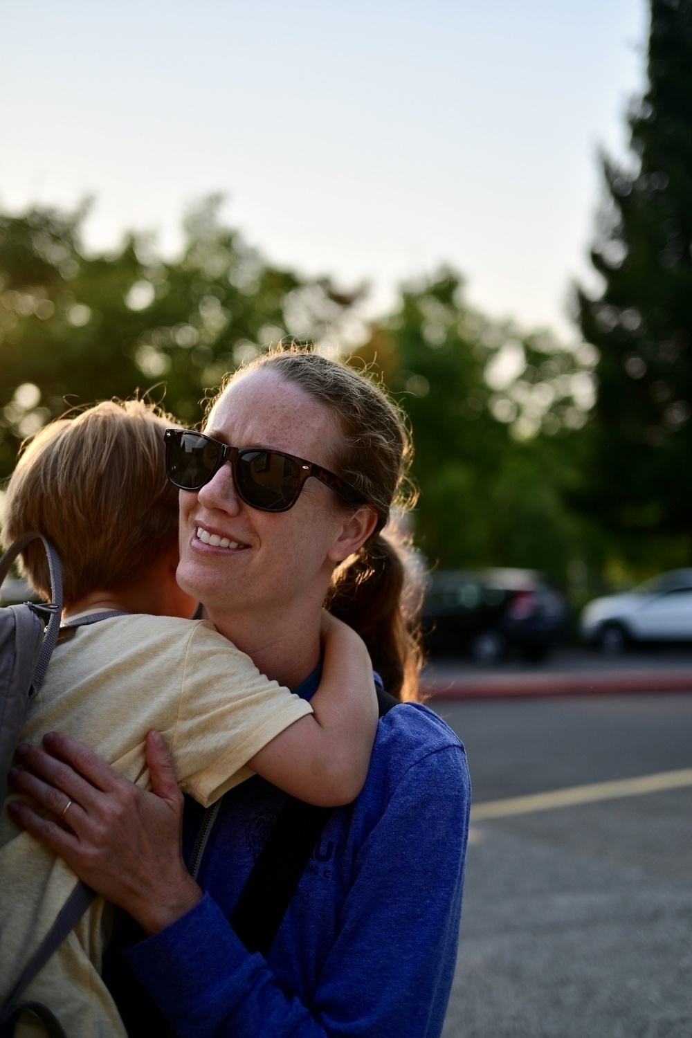 A woman wearing sunglasses is holding a young child in her arms outdoors.