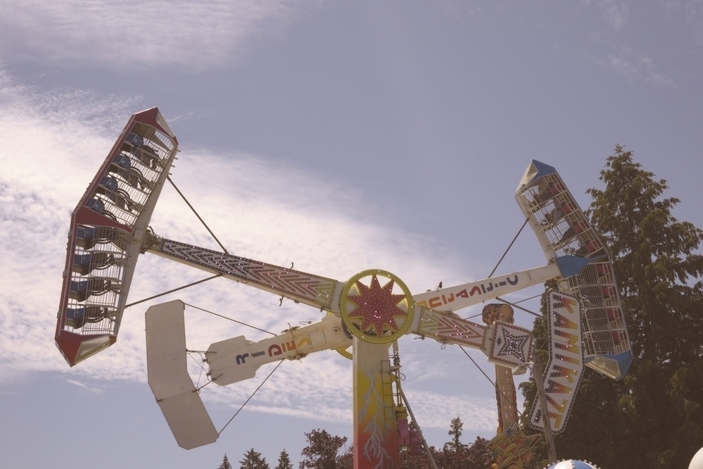 A spinning amusement park ride with passengers seated in separate compartments is set against a blue sky.