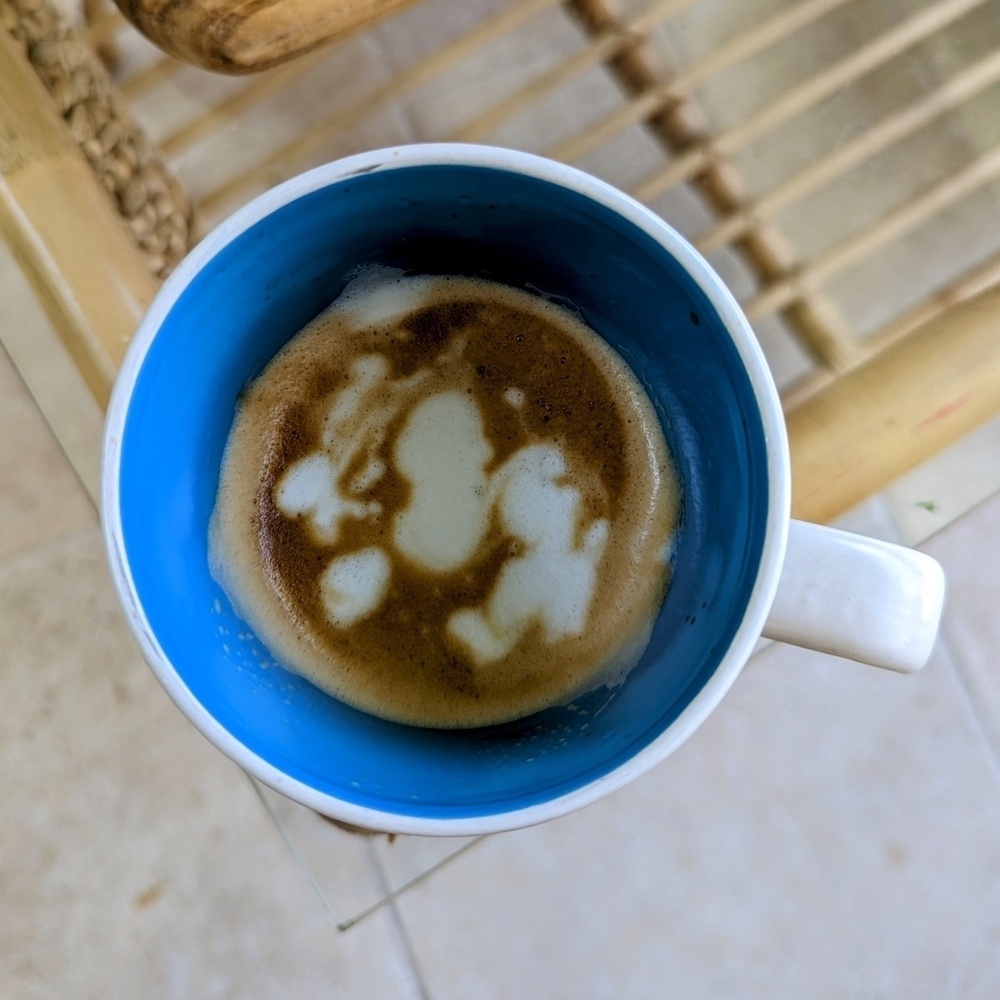 A mug of coffee viewed from above. The milk has been poured inexpertly in blobs.